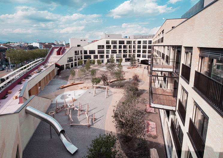 Erhöhter gemeinschaftlicher Hof mit Spielgeräten und Bäumen zwischen Wohnhäusern der Kalkbreite in Zürich